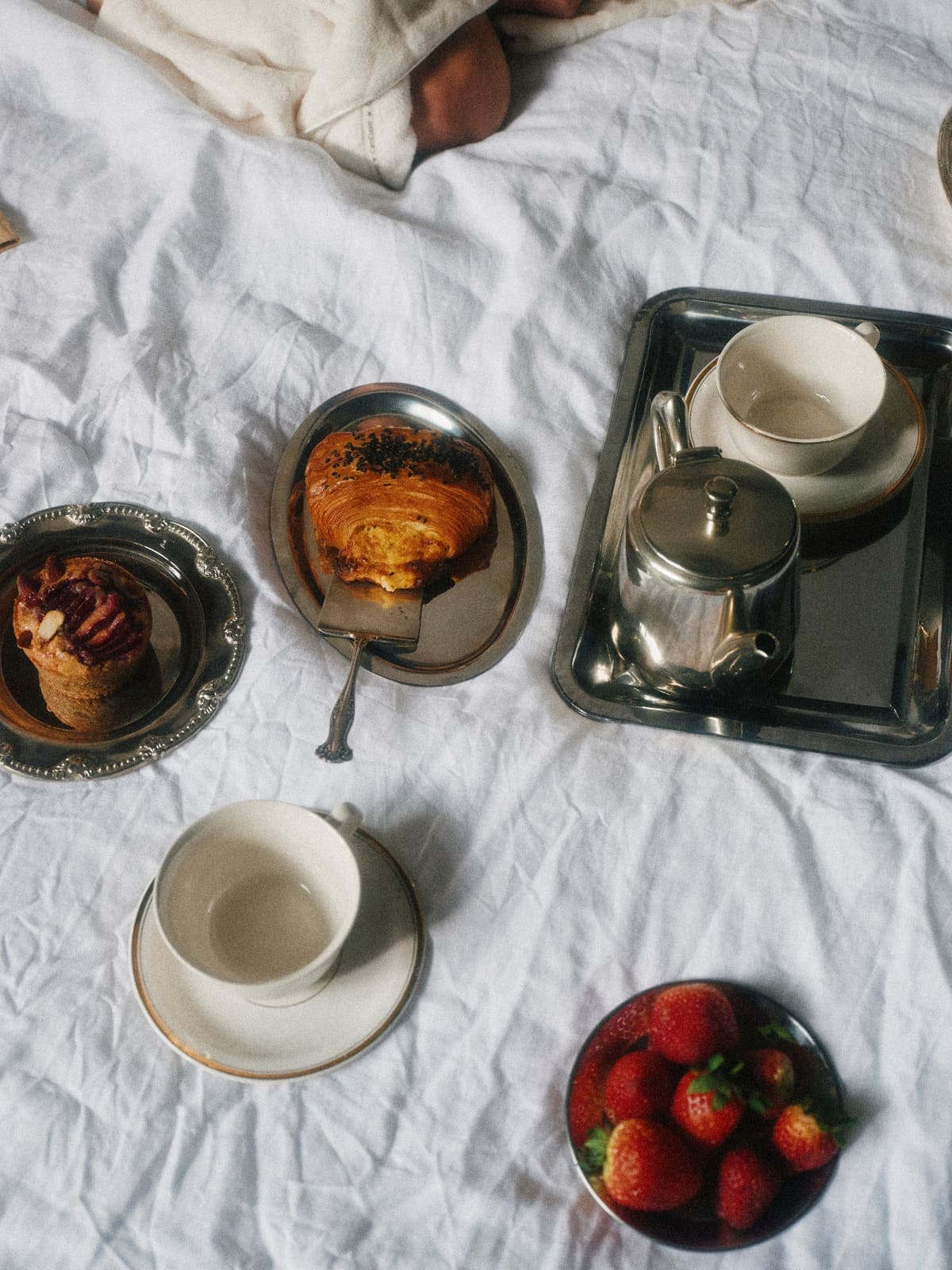 Breakfast set on white linen with silver trays.