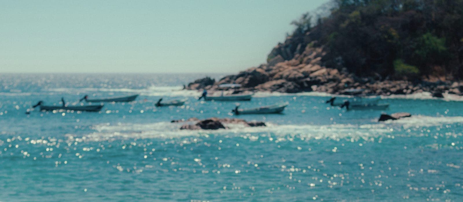 A seafront cove: small boats on turquoise water and granite rock, the Los Cabos coast.